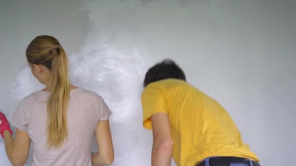 Een jonge man en vrouw zijn muren aan het renoveren in hun huis. Ze brengen klei aan op de muur. Zelf renoveren — Stockvideo