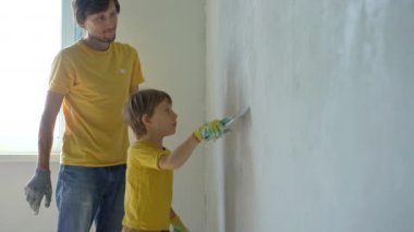 Genç bir adam ve oğlu evlerinde duvarları yeniliyorlar. Duvara macun sürüyorlar. Kendin tadilat yap. Çocuklara kendi başlarına nasıl tamir edeceklerini öğretmek.