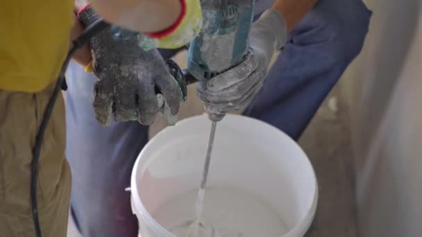 A young man and his son are doing a walls renovation in their home. They are mixing putty with a hand drill. Made renovation yourself. Teaching children how to do repairs by your own — Stock Video