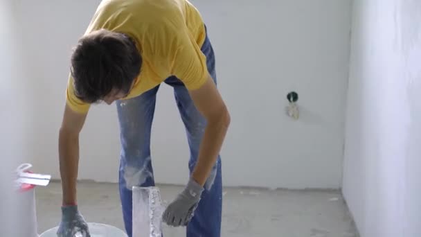 Un jeune homme portant un t-shirt jaune est en train de faire une rénovation de murs dans sa maison. Il applique du mastic sur le mur. Faire la rénovation vous-même — Video