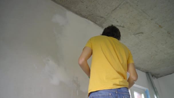 Een jonge man in een geel t-shirt is bezig met een renovatie van muren in zijn huis. Hij brengt klei aan op de muur. Zelf renoveren — Stockvideo