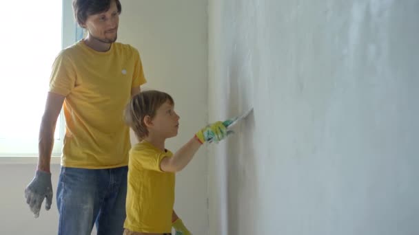 Mladý muž a jeho syn dělají ve svém domě renovaci zdí. Nanáší na zeď tmelu. Udělej si renovaci sám. Učit děti, jak se opravují sami — Stock video