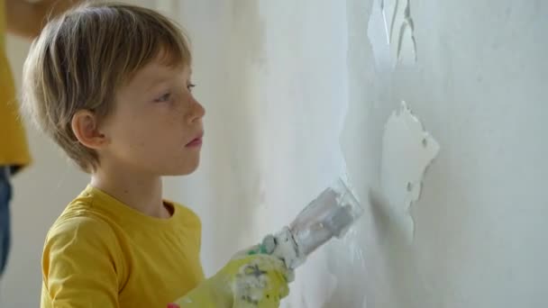 若い男と彼の息子は彼らの家の壁の改装を行っています。壁にパテを塗ります。自分で改装して。子供たちに自分で修理する方法を教える — ストック動画