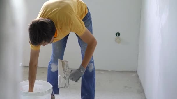 Een jonge man in een geel t-shirt is bezig met een renovatie van muren in zijn huis. Hij brengt klei aan op de muur. Zelf renoveren — Stockvideo
