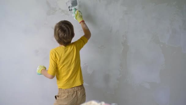 Un chico está aplicando masilla a la pared. Está bailando. Haz la renovación tú mismo. Enseñar a los niños a hacer reparaciones por su cuenta — Vídeos de Stock
