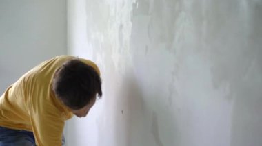 Sarı tişörtlü genç bir adam evinde duvar tadilatı yapıyor. O, macunu duvara uyguluyor. Tadilatı kendin yap.