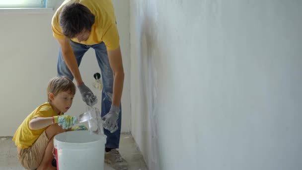 Молодий чоловік і його син роблять ремонт стін у своєму будинку. Вони наносять шпаклівку на стіну. Зроби сам ремонт. Навчання дітей робити ремонт самостійно — стокове відео