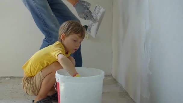 Ein junger Mann und sein Sohn renovieren gerade eine Mauer in ihrem Haus. Sie tragen Kitt auf die Wand auf. Renovieren Sie selbst. Kindern beibringen, wie man Reparaturen selbst durchführt — Stockvideo