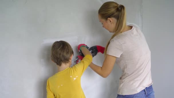 Una giovane donna e suo figlio stanno ristrutturando le pareti della loro casa. Stanno applicando lo stucco al muro. Rinnovati da solo. Insegnare ai bambini come fare le riparazioni da soli — Video Stock