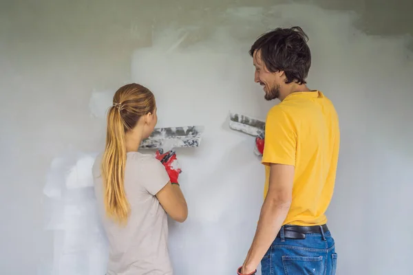 Mężczyzna i kobieta tynkują ściany w domu. Remont domu DIY — Zdjęcie stockowe