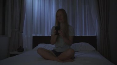 Geceleri bir kadın, uyumadan önce dinlenmek için meditasyon ve telefonundaki rahatlama uygulamasını açar. Stres önleyici uygulamalar. Sağlıklı bir yaşam tarzı. Yeni normal