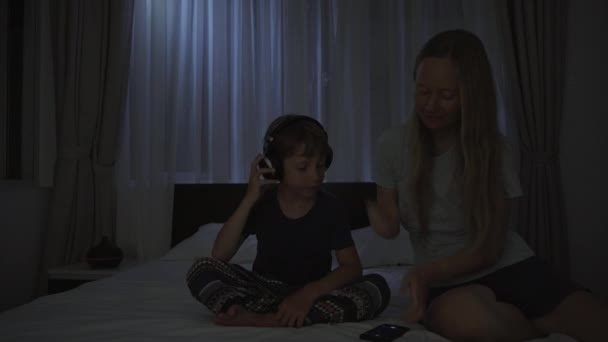 La nuit, une femme met en marche une application de méditation et de relaxation sur son téléphone pour que son fils puisse se détendre avant d'aller se coucher. Applications anti-stress. Mode de vie sain. Nouvelle normalité — Video