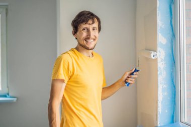 Bir erkek boyacı boyacı boya ve boya silindiriyle duvar astar. ÇEVİR