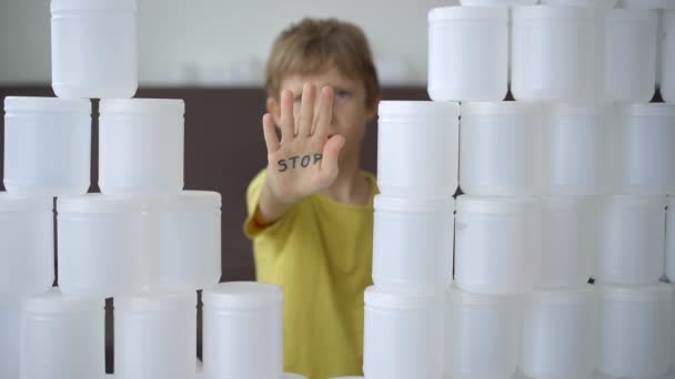 Een jongen met een belettering stop op zijn hand breekt omringd door een muur van plastic blikjes. Stop plastic vervuiling. Verminder kunststoffen voor eenmalig gebruik. Langzame video — Stockvideo