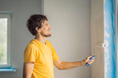Bir erkek boyacı boyacı boya ve boya silindiriyle duvar astar. ÇEVİR