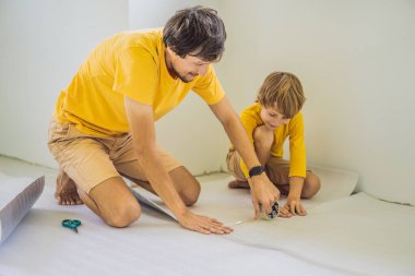 Baba ve oğul yer yalıtımı yapıyorlar. Kaplamalı ahşap döşeme için yalıtkan kumaş rulosu