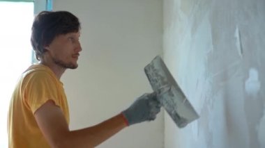 Sarı tişörtlü genç bir adam evinde duvar tadilatı yapıyor. O, macunu duvara uyguluyor. Tadilatı kendin yap.