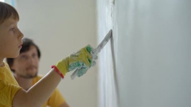 Genç bir adam ve oğlu evlerinde duvarları yeniliyorlar. Duvara macun sürüyorlar. Kendin tadilat yap. Çocuklara kendi başlarına nasıl tamir edeceklerini öğretmek.