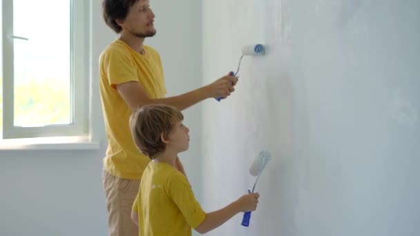 Genç bir adam ve oğlu evlerinde duvarları yeniliyorlar. Duvarı boya silindirleriyle boyuyorlar. Kendin tadilat yap. Çocuklara kendi başlarına nasıl tamir edeceklerini öğretmek. — Stok video
