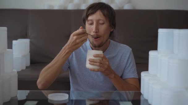 Un homme mange du yaourt dans une boîte en plastique blanche. La caméra se déplace et révèle qu'il y a une pile de canettes en plastique vides autour de lui. Arrêtez la pollution plastique. Réduire les plastiques à usage unique. Écologique — Video