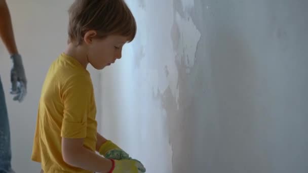 A young man and his son are doing a walls renovation in their home. They are applying putty to the wall. Make renovation yourself. Teaching children how to do repairs by your own — Stock Video