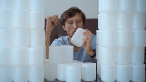 Un uomo è seduto davanti a un muro fatto di lattine di plastica. È inorridito dalla quantità di plastica che deve smaltire. Fermare l'inquinamento di plastica. Ridurre la plastica monouso — Video Stock