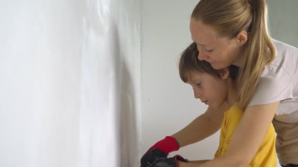 A young woman and her son are doing a walls renovation in their home. They are applying putty to the wall. Make renovation yourself. Teaching children how to do repairs by your own — Stock Video
