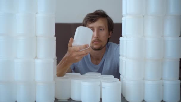 Un hombre está sentado frente a una pared hecha de latas de plástico. Está horrorizado por la cantidad de plástico que tiene que disponer. Detener la contaminación plástica. Reducir los plásticos de un solo uso — Vídeo de stock