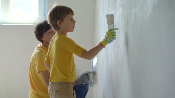 Ein junger Mann und sein Sohn renovieren gerade eine Mauer in ihrem Haus. Sie tragen Kitt auf die Wand auf. Renovieren Sie selbst. Kindern beibringen, wie man Reparaturen selbst durchführt — Stockvideo