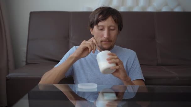 Seorang pria makan yogurt dari kaleng plastik putih. Kamera bergerak dan mengungkapkan bahwa ada tumpukan kaleng plastik kosong di sekelilingnya. Hentikan polusi plastik. Mengurangi plastik sekali pakai. Ekologi — Stok Video