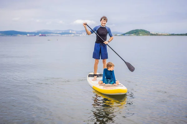 Vater und Sohn paddeln auf Stand Up Board und haben Spaß im Sommerurlaub am Strand — Stockfoto