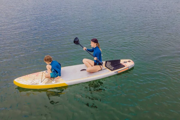 Mutter und Sohn paddeln auf Stand Up Board und haben Spaß im Sommerurlaub am Strand — Stockfoto