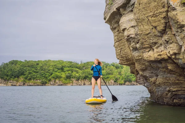 Jovens mulheres se divertindo Stand Up Paddling no mar. SUP. Menina de cabelo vermelho Treinamento em Paddle Board perto das rochas — Fotografia de Stock