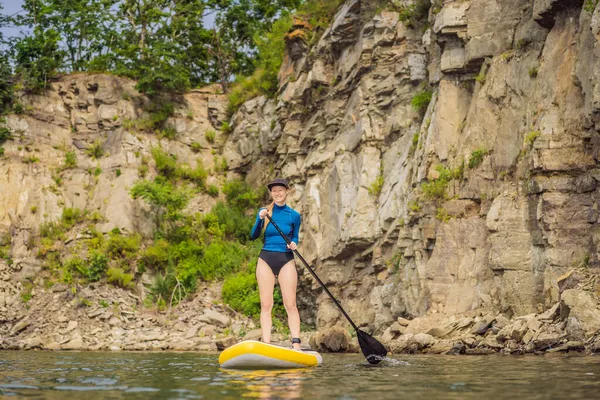 Jonge vrouwen met plezier stand-up peddelen in de zee. Een SUP. Rood haar meisje training op peddel boord in de buurt van de rotsen — Stockfoto