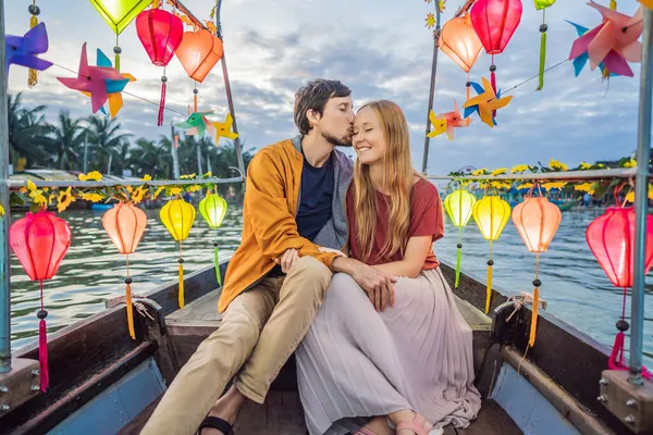 Ευτυχισμένο ζευγάρι των ταξιδιωτών βόλτα ένα εθνικό σκάφος στο παρασκήνιο του Hoi An αρχαία πόλη, Βιετνάμ. Βιετνάμ ανοίγει για τους τουρίστες και πάλι μετά την καραντίνα Coronovirus COVID 19 — Φωτογραφία Αρχείου