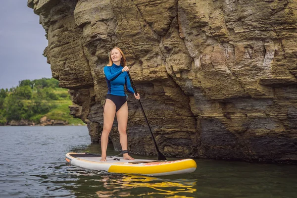 Młode kobiety mają zabawy Stand Up Wiosłując w morzu. SUP. Rude włosy dziewczyna Trening na Paddle Board w pobliżu skał — Zdjęcie stockowe