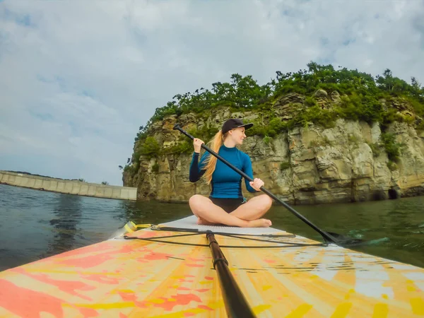 Jonge vrouwen met plezier stand-up peddelen in de zee. Een SUP. Rood haar meisje training op peddel boord in de buurt van de rotsen — Stockfoto