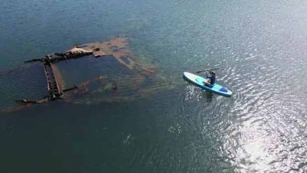 ยิงทางอากาศ หญิงสาวกําลังสนุก ลุกขึ้นยืน Paddling ในทะเล ซูเปอร์ การบุกรุกท่ามกลางหนี้สินของเรือโลหะจม — วีดีโอสต็อก