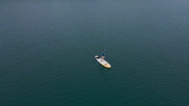 Hava görüntüsü. Genç kadınlar eğleniyor. Denizde kürek çekerek ayağa kalk. - Süper. Kızıl saçlı kız kayaların arasında kürek çekiyor.