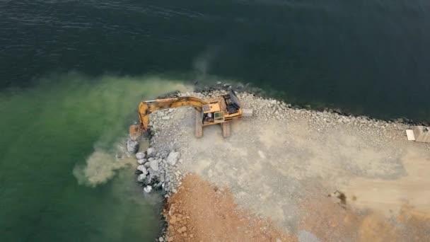 空中ビデオ。海の中に土地を構築する上で働く上と掘削機からの眺め。石で海岸を埋める。海岸線強化、浸食制御、海面上昇との戦い。海岸線 — ストック動画