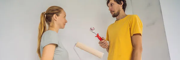 BANNER, LONG FORMAT A man and a woman with rollers for painting the walls. A man with a very small bolster, symbolizing a small penis. renovation diy paint couple in new home painting wall — Stok fotoğraf