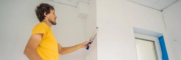 Ein männlicher Hausmaler arbeitet beim Streichen und Grundieren der Wand mit einer Malerrolle. DIY BANNER, LONG FORMAT — Stockfoto