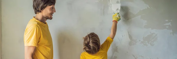 L'uomo con suo figlio fa riparazioni a casa, insegna ai bambini a intonacare le pareti con una spatola in mano BANNER, FORMATO LUNGO — Foto Stock