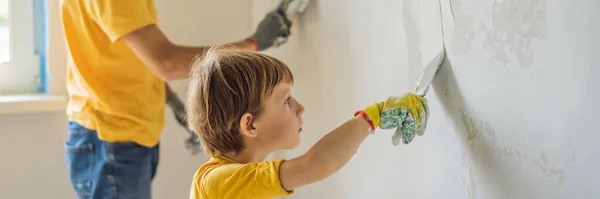 Мужчина с сыном ремонтирует дома, учит детей штукатурить стены шпателем в руках БАННЕР, ДЛЯ ФОРМАТА — стоковое фото