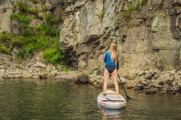 Junge Frauen haben Spaß beim Stand Up Paddling im Meer. SUP. Mädchen mit roten Haaren trainiert auf Paddelbrett in der Nähe der Felsen — Stockfoto