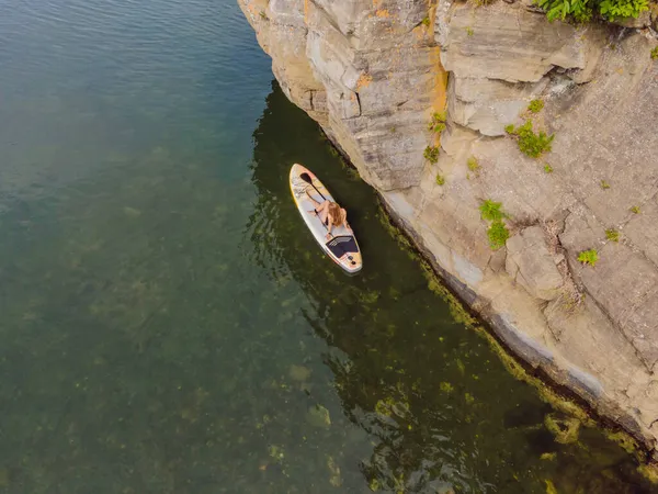 Молоді жінки, маючи веселощі, пливуть морем. НОП. Червоноволоса дівчинка Тренування на Paddle Board поруч з камінням — стокове фото