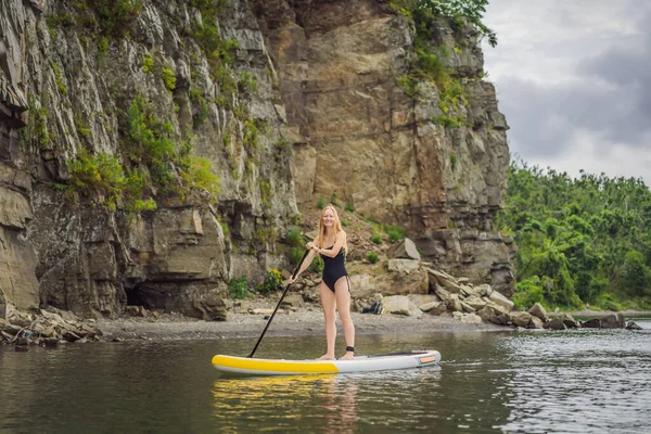 Giovani donne che si divertono Stand Up Paddling nel mare. SUP. Rosso capelli ragazza Formazione su Paddle Board vicino alle rocce — Foto Stock