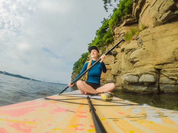 Junge Frauen haben Spaß beim Stand Up Paddling im Meer. SUP. Mädchen mit roten Haaren trainiert auf Paddelbrett in der Nähe der Felsen — Stockfoto