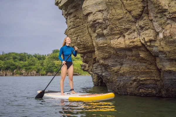 Jovens mulheres se divertindo Stand Up Paddling no mar. SUP. Menina de cabelo vermelho Treinamento em Paddle Board perto das rochas — Fotografia de Stock