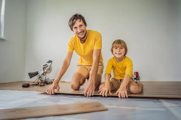 Far och son installera nya trä laminatgolv på en varm film golv. infraröd golvvärmesystem under laminatgolv — Stockfoto